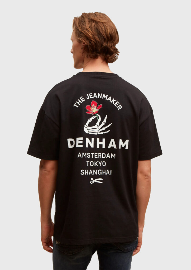 A man wearing a black t-shirt. It is a view from behind and the shirt contains a skeleton hand holding a flower. There is typography surrounding it.