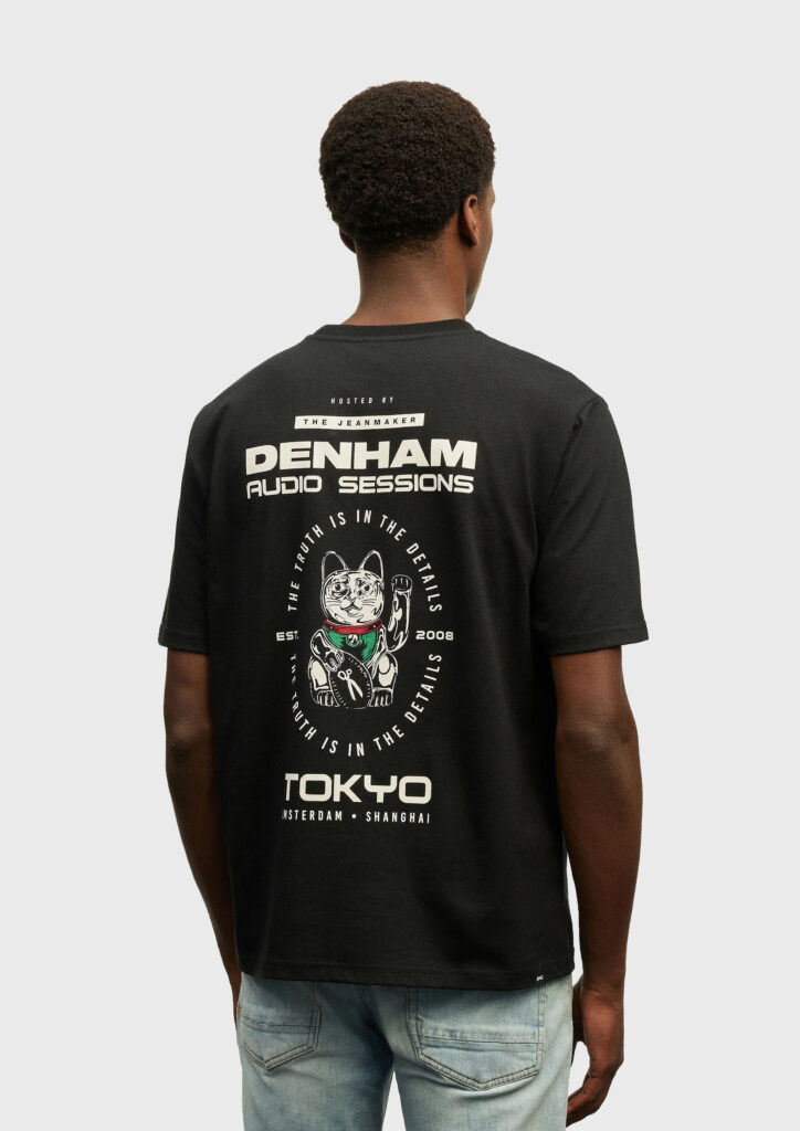 A reverse shot of a man wearing a Denham shirt. The shirt is black and feature an illustration of a Japanese 'lucky cat', and some typography.